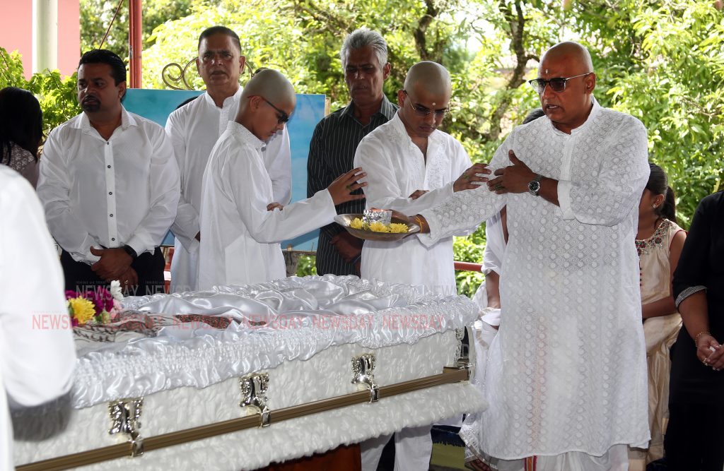 Works and Transport Minister Rohan Sinanan right  perform aarti at the casket of hismother Lelamatie Sinanan during the  funeral service at their family home at Guaico Junction, Sangre Grande. PHOTO SUREASH CHOLAI