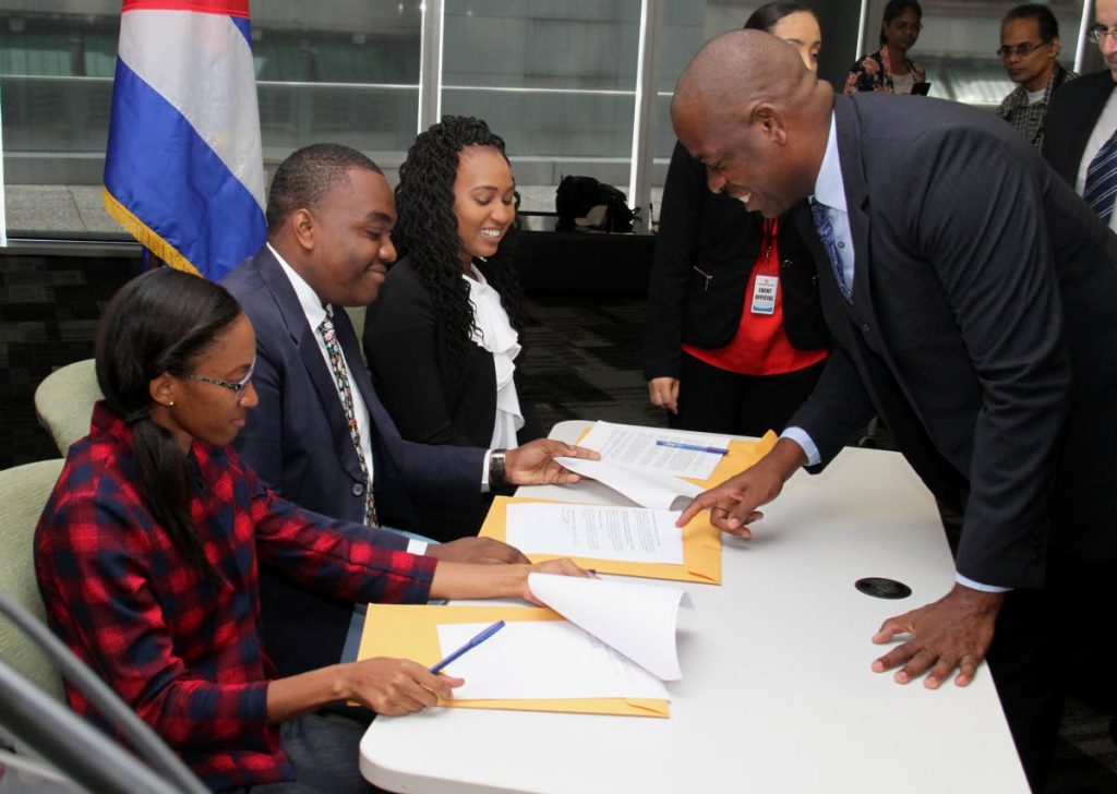 Minister in the Ministry of Education Lovell Francis with Cuba scholarship recipients, from left, Andrea Branche, Manasseh Mark and Radannia Picou as they sign the code of ethics at the Cuban scholarship signing ceremony at the Education Towers, Port-of-Spain on Friday. PHOTO BY AYANNA KINSALE