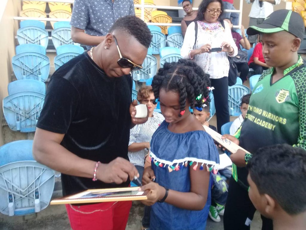 Trinbago Knight Riders captain Dwayne Bravo, left, signs autograghs for children at the Newsday Kids meet and greet session at the Queen's Park Oval in St Clair, yesterday.