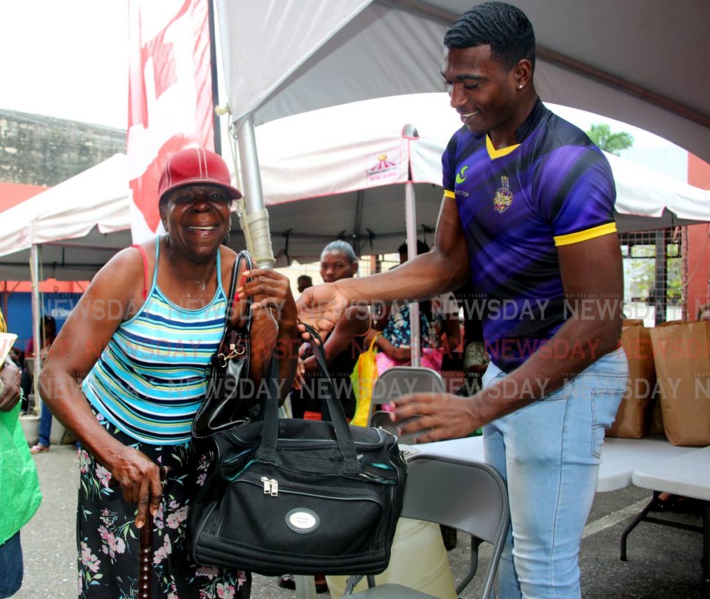 St Kitts and Nevis pacebowler Sheno Berridge who is part of the Trinbago Knight Riders' (TKR) contingent hands a food hamper to Claudia Enill while doing volunteer work at the Living Water Community , Frederick Street , Port of Spain. PHOTO SUREASH CHOLAI