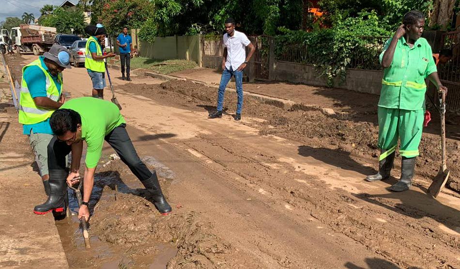 HELPING HAND: Local Govt Minister Kazim Hosein shovels up mud during clean-up exercises yesterday in Mt Lambert. PHOTOS COURTESY LOCAL GOVT MINISTRY