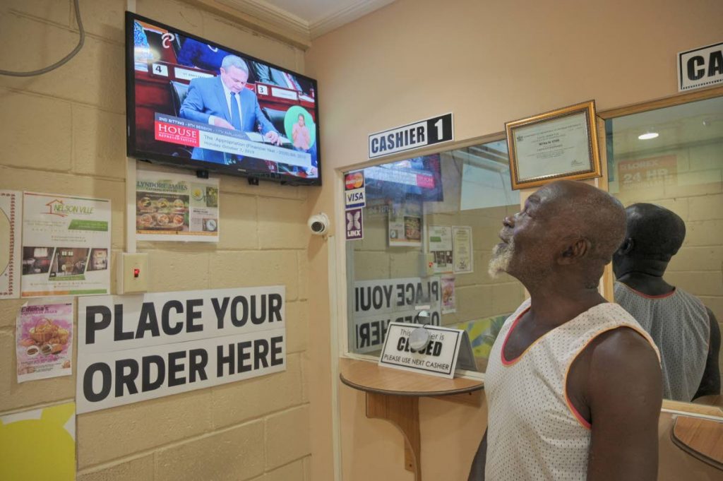 A customer at Visto Enterprises in Shaw Park, Tobago listens to Finance Minister Colm Imbert as he presents the 2019/2020 budget on Monday. PHOTO BY LEEANDRO NORAY