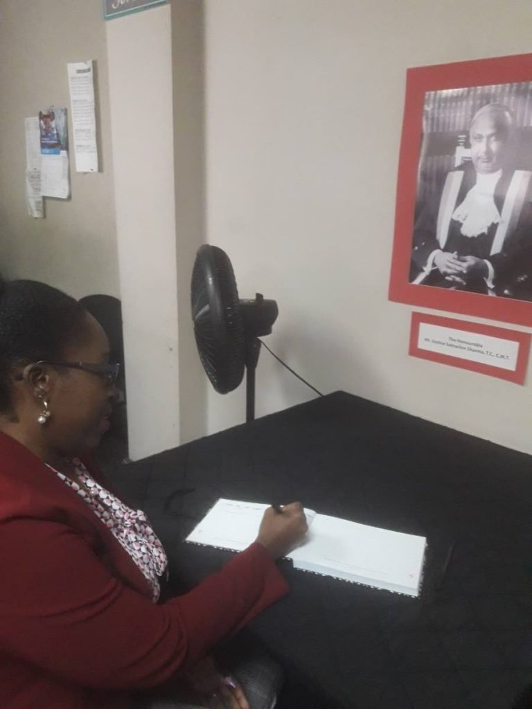 Jacqueline Lewis, Court Customer Relations representatives, at San Fernando Supreme court, signs the condolence book in memory of former Chief Justice Sat Sharma. He died last week Wednesday