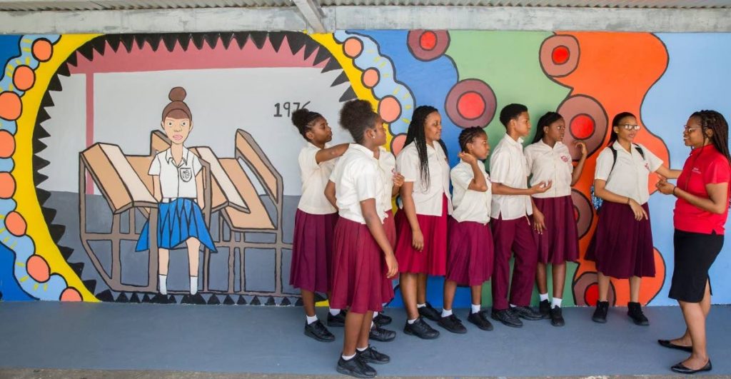 MURAL UNVEILED: Digicel Foundation strategic partnership officer Alicia Hospedales shares a word with students in front of their painted mural which depicts the very first uniform worn by students when the school opened in 1976.  - 