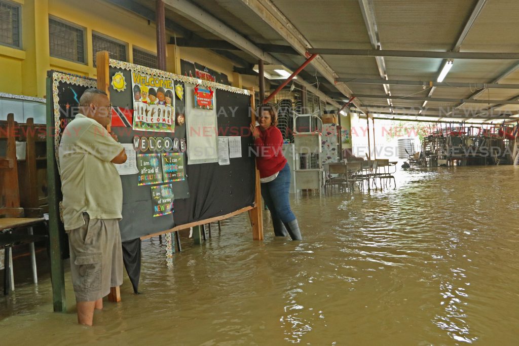 Principal of Debe Hindu SDMS Primary School Usha Rampersad-Gookool gets assistance to move school board out of flood waters on Tuesday afternoon.
Photo by Marvin Hamilton.