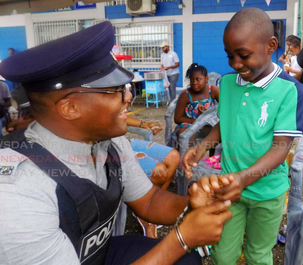 Roshawn Alexander, 7, places PC O'Neil of the Port of Spain City Police in handcuffs at the fourth annual Port of Spain City Police Christmas Party on Sunday - Shane Superville