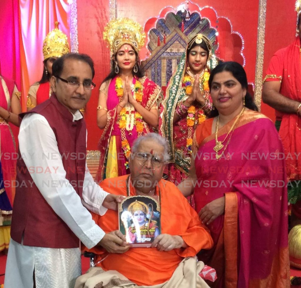 Professor Hari Shanker Adesh, sitting, holds his book Raghuvansh Shiromani Shri Raam, with his son pandit Vivek Adesh, left, and daughter-in-law Shrimati Kadambari Adesh, right. In the background are actors who took part in a drama during the book's launch at Shri Adesh Ashram, Aranjuez.
 - 