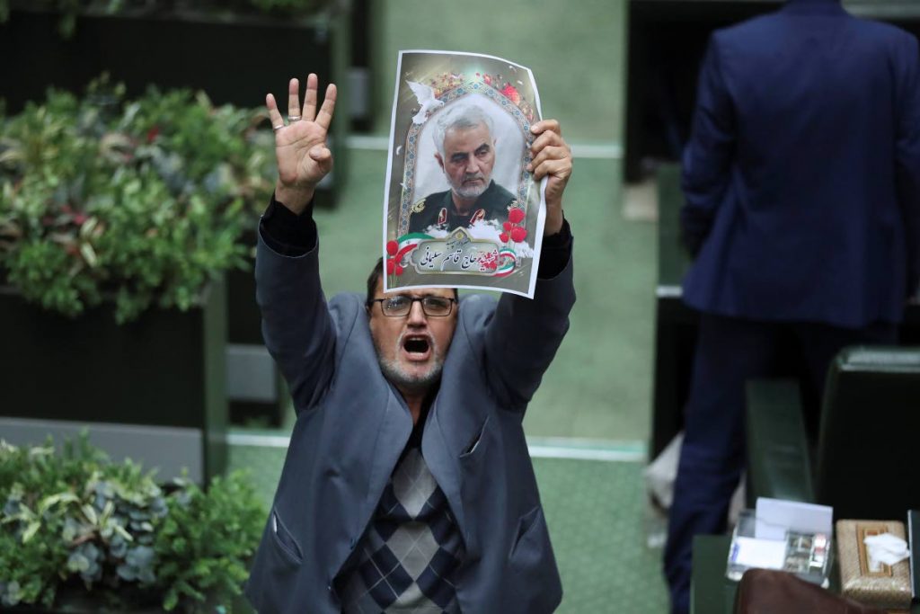 Iranian lawmaker Mohammad Javad Abtahi encourages his colleagues to vote for a bill as he holds a poster of Gen Qassem Soleimani, who was killed in Iraq in a US attack, in an open session of parliament, in Tehran, Iran on Tuesday. - Vahid Salemi