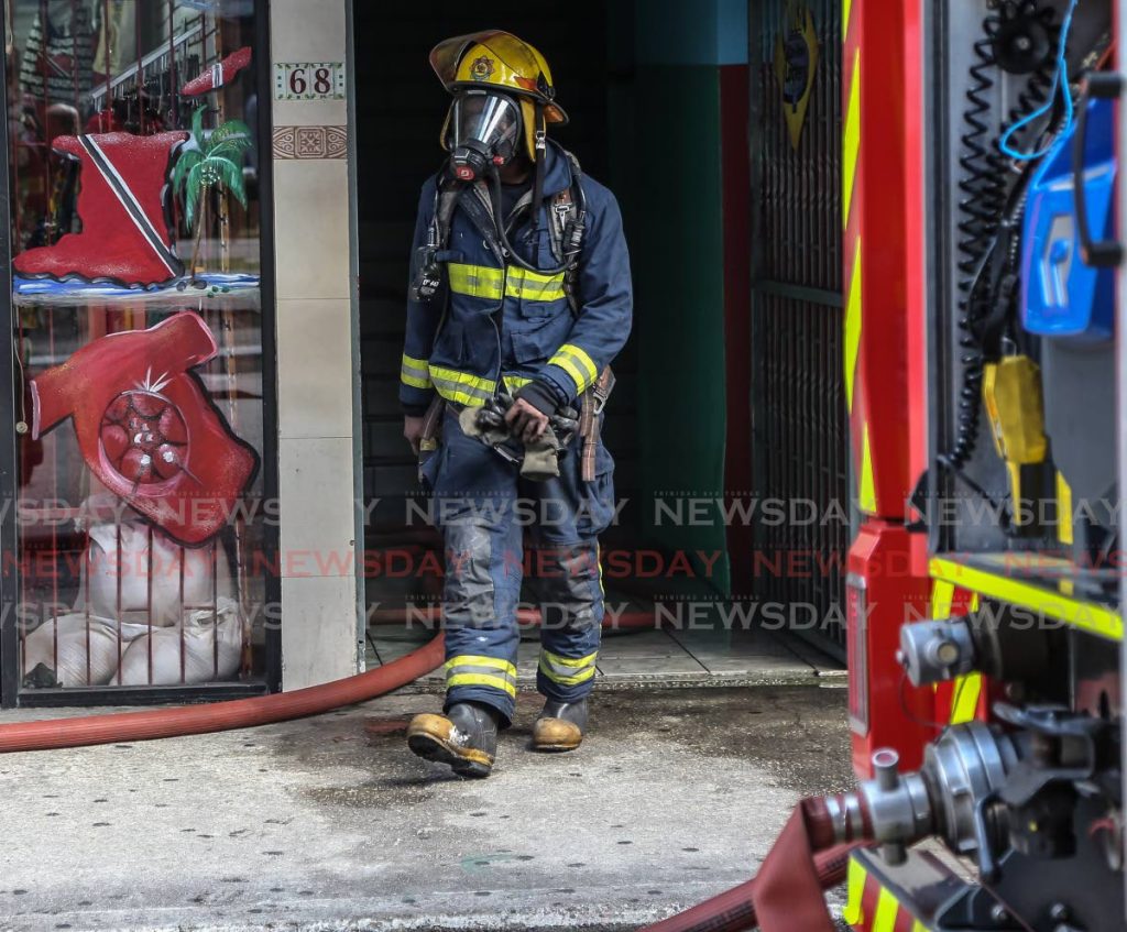 Fire officers with Self Contained Breathing Apparatus (SCBA) emerge from the building after containing the fire which started in D' Bocas bar Independence Square, Port of Spain. - Jeff Mayers