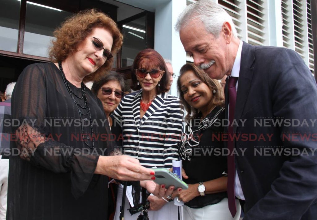 SAD KIND OF JOY: Relatives and friends, despite their grief, manage smiles as they look at a cellphone photo of artist and historian Adrian Camps-Campins after his funeral on Friday at the Church of the Assumption in Maraval. - Ayanna Kinsale