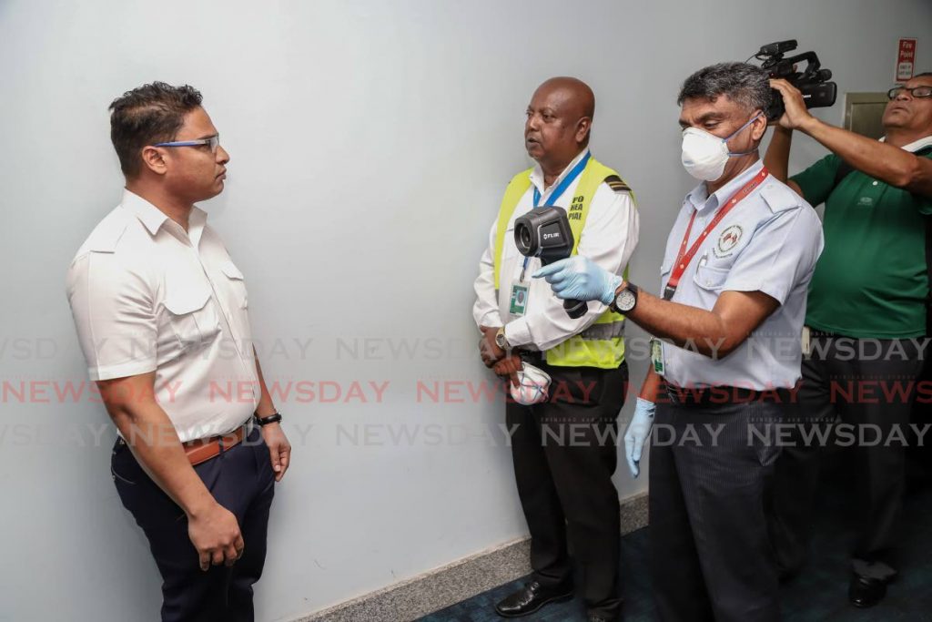 Public health inspector Nirmal Buchoon demonstrates one of the way passengers at the 
Piarco airport are screened for elevated temperatures as part of the coronavirus protocols in place. 
PHOTO BY JEFF K MAYERS - 