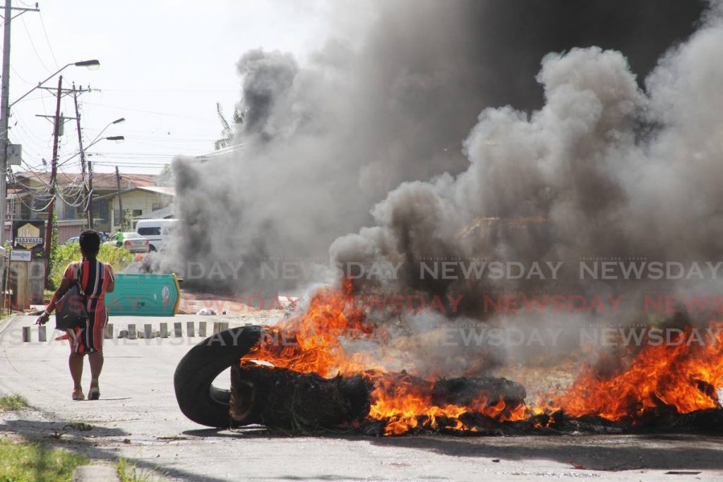 File photo: A woman walks past a fire set by residents on the road near Perry Young Road, Indianwalk, Moruga in February. Residents are protesting poor road conditions.


 - L Holder