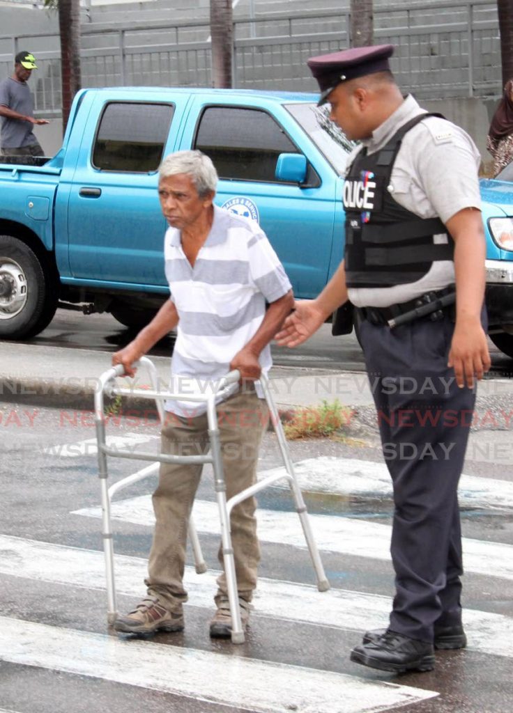 In this file photo a police officer assists an elderly man cross the street in San Fernando. Old age pensions may barely cover the living expenses of beneficiaries, especially those with health problems.