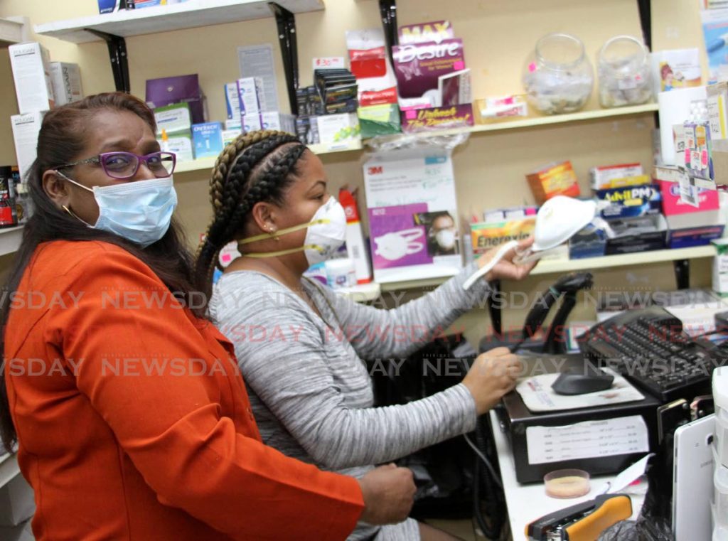 MASKED: Quik Pharm Pharmacy, employees Davi Satram and Anneshia Aguillera, right. wearing face masks on the job on Wednesday. Aguillera cashes for a face mask purchased by a customer.  - Angelo Marcelle