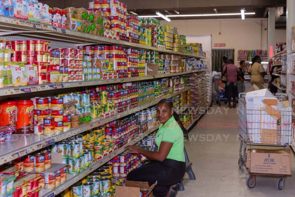 FULLY STOCKED: An employee at Penny Savers, Bon Accord packs goods on shelves on Thursday while customers do their shopping. Penny Savers' competitior Viewport Supermarket on Thursday said it was temporarily closing as a precaution against covid19 but reopened a day later.  - DAVID REID