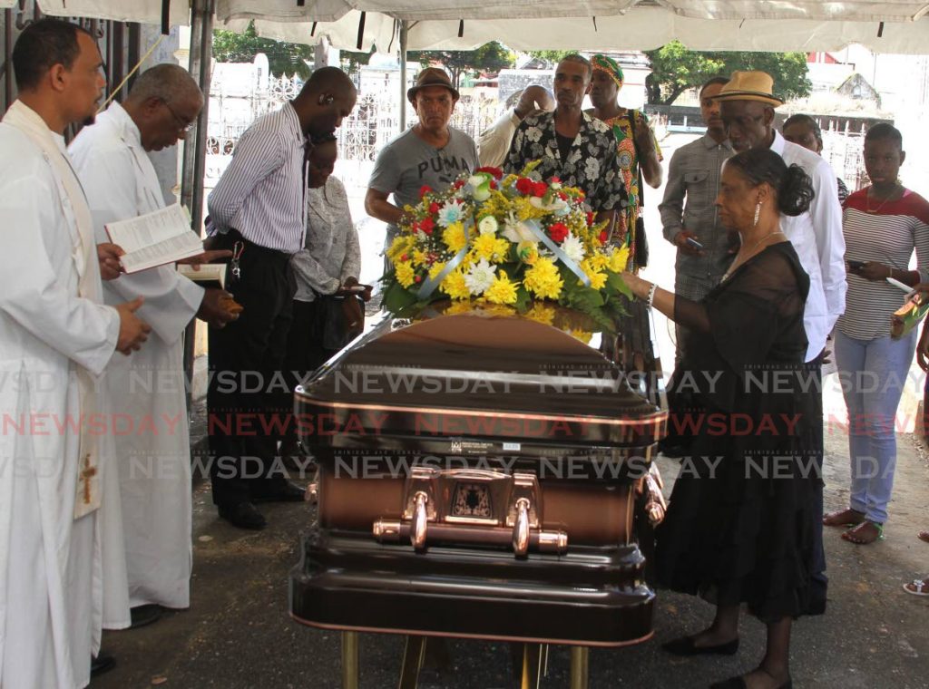 Ingrid Jules touches her husband Neville Jules' casket as prayers are said at the Lapeyrouse cemetery prior to his burial on Friday.  PHOTO BY AYANNA KINSALE - Ayanna Kinsale