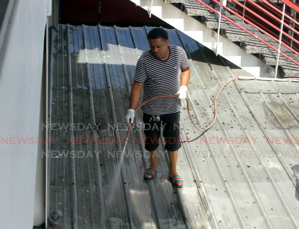 Maxi driver Ryan Strong uses a power washer to clean the railings at City Gate, Port of Spain, to help control the spread of the covid19. - Ayanna Kinsale