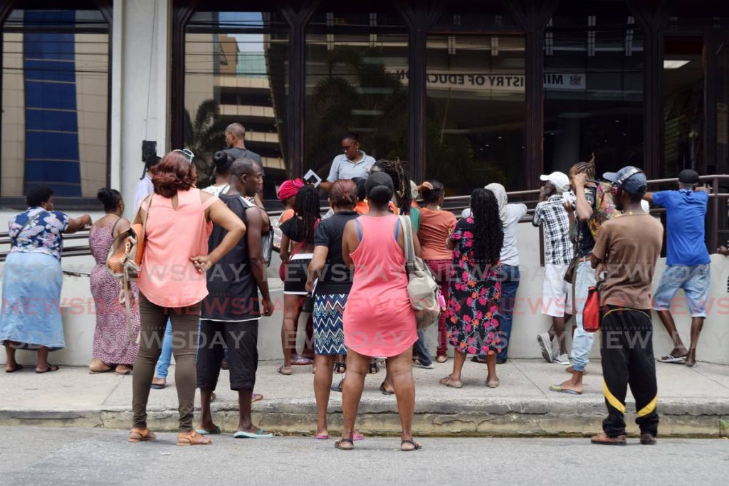 People gather at the entrance to TTPOST on St Vincent Street, Port of Spain, on Tuesday as a postal worker calls out names for people to collect pension and other cheques. - Vidya Thurab