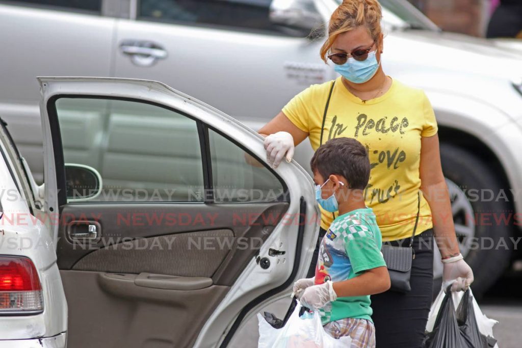 File photo: A boy helps with the bags while going into a vehicle with a woman as they both wear masks and gloves, in San Fernando. - MARVIN HAMILTON