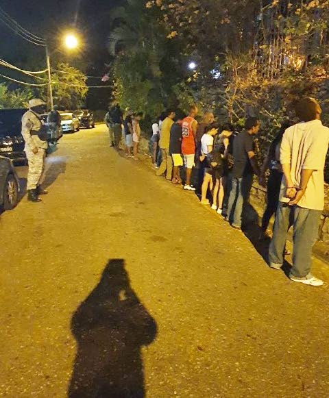 IN TROUBLE: The men who were have a great time in a covid19 fete before police crashed it, are lined up along the road before being taken away by officers. PHOTO COURTESY TTPS - TTPS