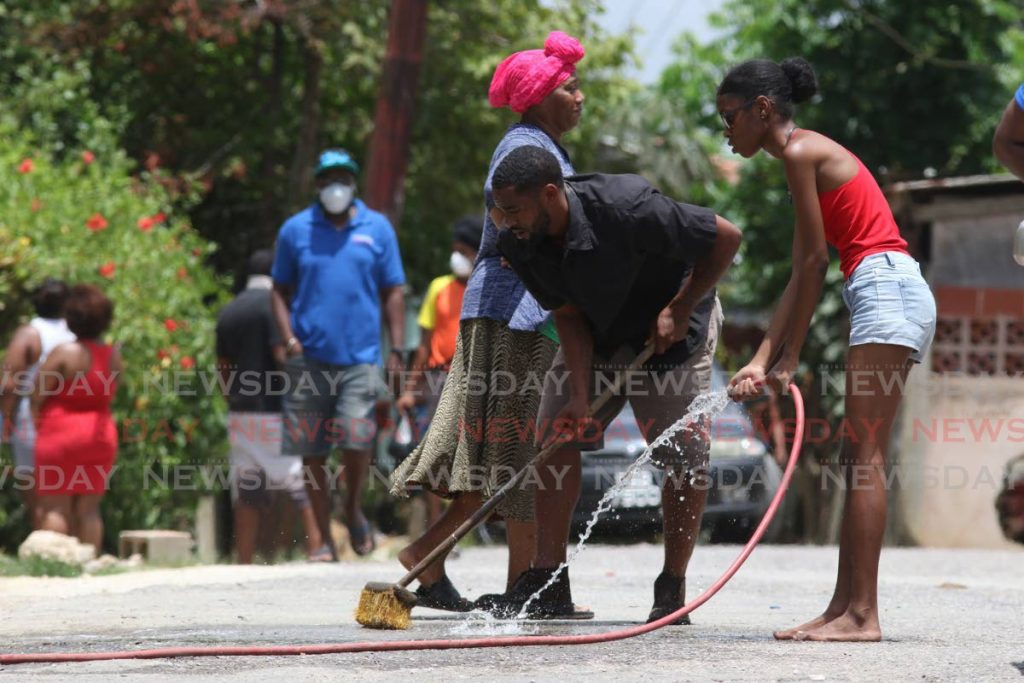 Residents of Silk Cotton Road, Battoo Avenue, Marabella wash away bloodstains on the road where Desmond Edwards was gunned down on Saturday morning. PHOTO BY MARVIN HAMILTON - 