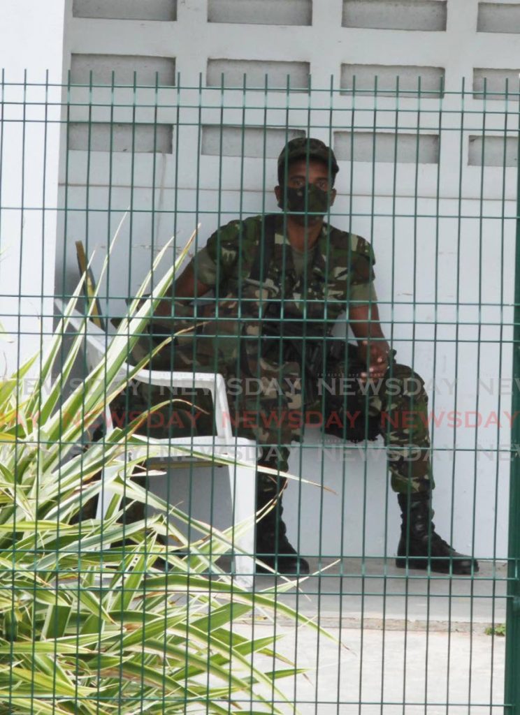 A soldier watches over members of Kingdom Wealth prayer group as it prays outside the Couva Hospital and Multi-Training Facility on the Sir Solomon Hochoy Highway on Sunday. - Vashti Singh