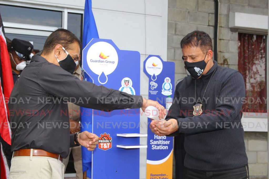 COME WITH CLEAN HANDS: Guardian Group Director Ravi Tewarie pours hand sanitiser in Police Commissioner Gary Griffith’s hands on Monday during a handing over ceremony of hand sanitiser dispensers at the Woodbrook Police Station - ROGER JACOB