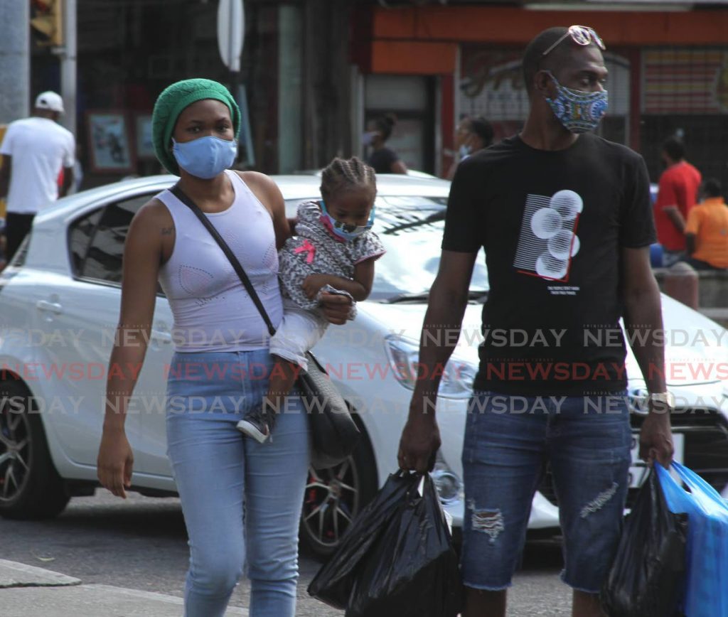 File photo: A woman holding a child and a man, all wearing face masks, walk through Port of Spain. - Ayanna Kinsale