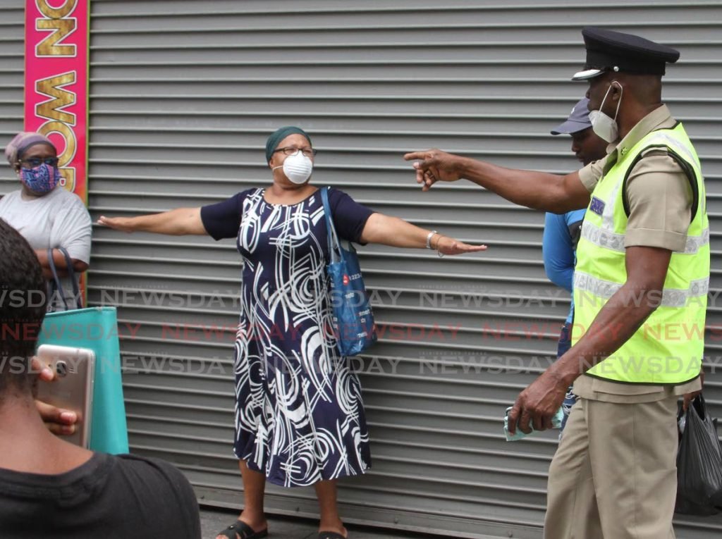A woman uses her arms length, to obey the social distancing instructions of Senior Superintendent Daniel Moore, as he and other offices of the Port of Spain Division, patrolled Charlotte Street on Friday. - ANGELO MARCELLE