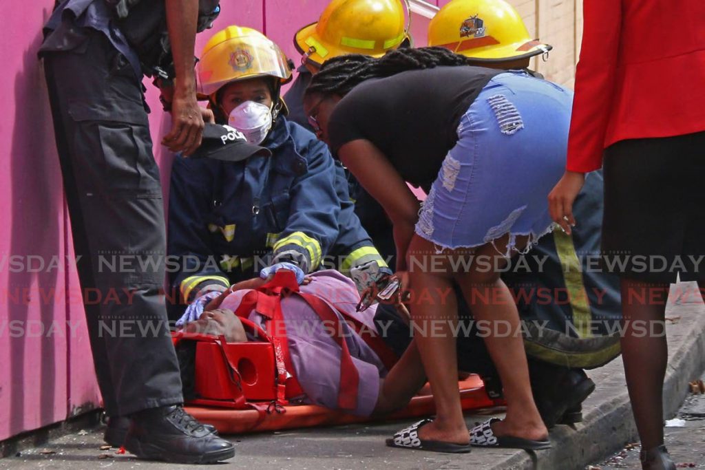 Police, fire officers, ambulance personnel and passers by assist a woman after she was knocked down on Penitence Street, San Fernando, on Monday. - Marvin Hamilton