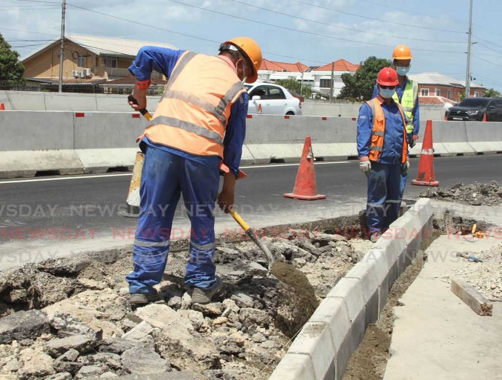 A masked worker puts cement on some bricks at the Curepe interchange on the Churchill Roosevelt Highway.   - Ayanna Kinsale