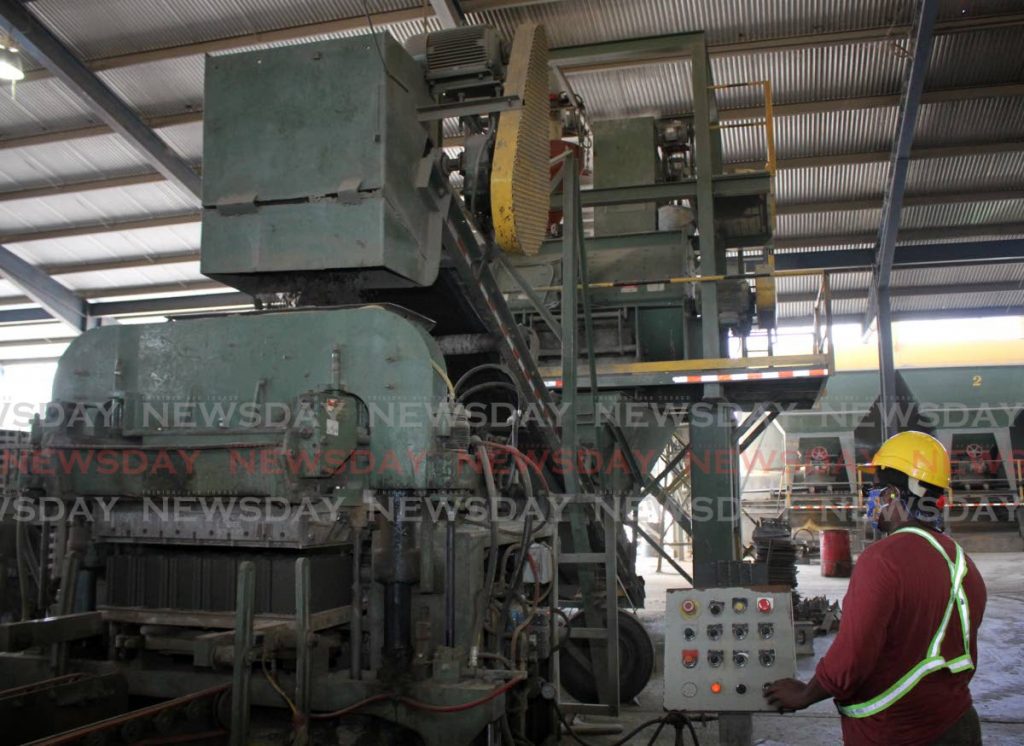 An employee at Coosal's Construction Co Ltd works on a block-making machine at a factory in Cunupia on May 21. Economists say the TT economy has to be 