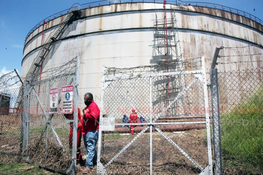 Wokers look on as an assessment is done on a storage tank which ruptured, spilling hundreds of gallons of salt water onto a nearby roadway, at Clifton Hill, Point Fortin. - Lincoln Holder