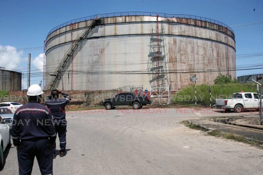 Workers look on as an assessment is done on a storage tank which ruptured spilling hundreds of gallons of salt water onto a nearby roadway at Clifton Hill, Point Fortin on Sunday.  PHOTO BY LINCOLN HOLDER - Lincoln Holder