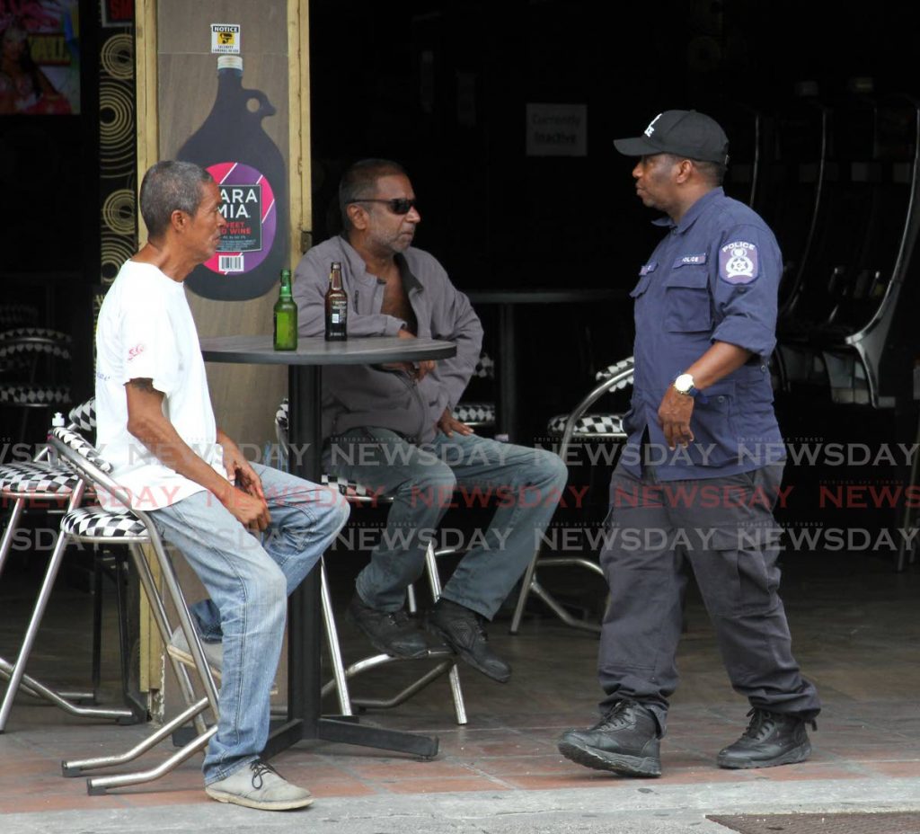 In this file photo a policeman walks past men drinking at a bar on Western Main Road, St James on June 22. - Angelo Marcelle