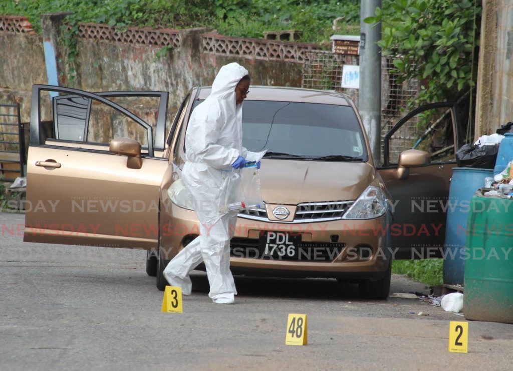 A crime scene investigator gathers clues at the scene where three men were shot dead by police in Morvant on June 27. - ROGER JACOB