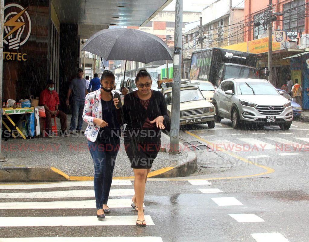 File photo of ladies sharing an umbrella as they shelter the rain on Frederick Street, Port of Spain.  - Ayanna Kinsale