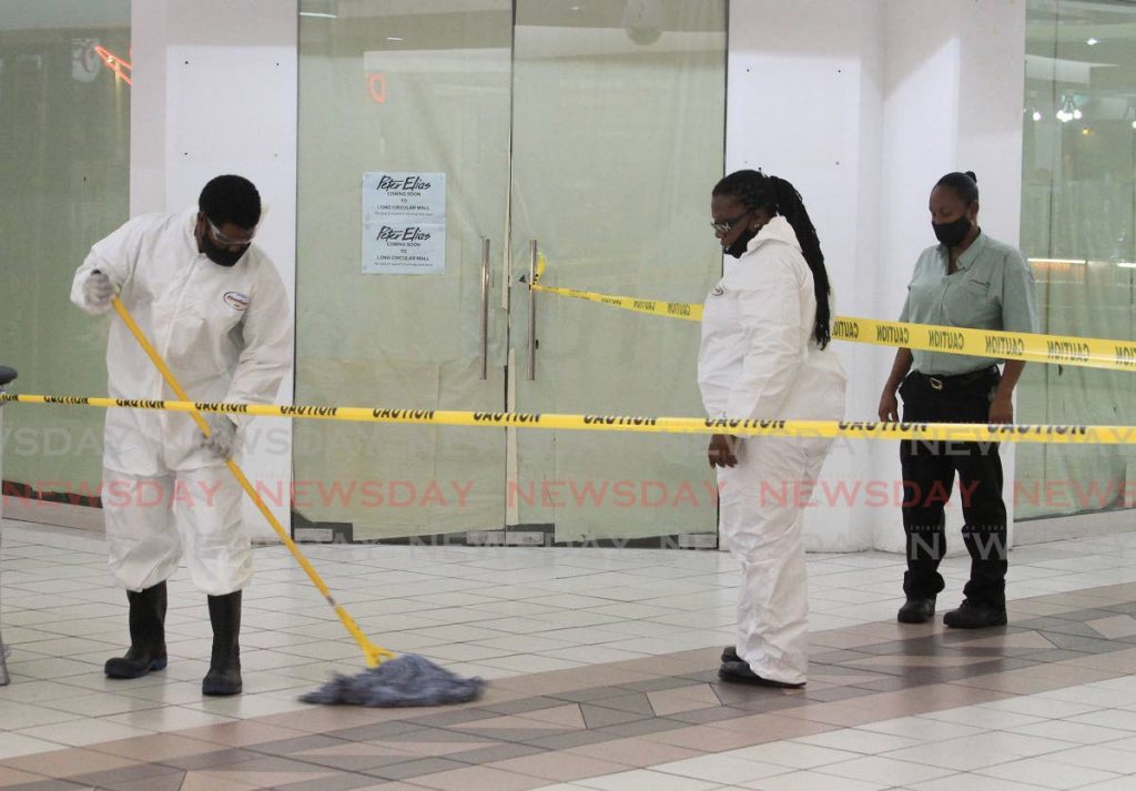 Workers, wearing personal protective equipment, sanitise the floors at Long Circular Mall after a customer suspected of coming into contact with a covid19-positive person visited the mall's Pennywise branch.  PHOTO BY AYANNA KINSALE - 