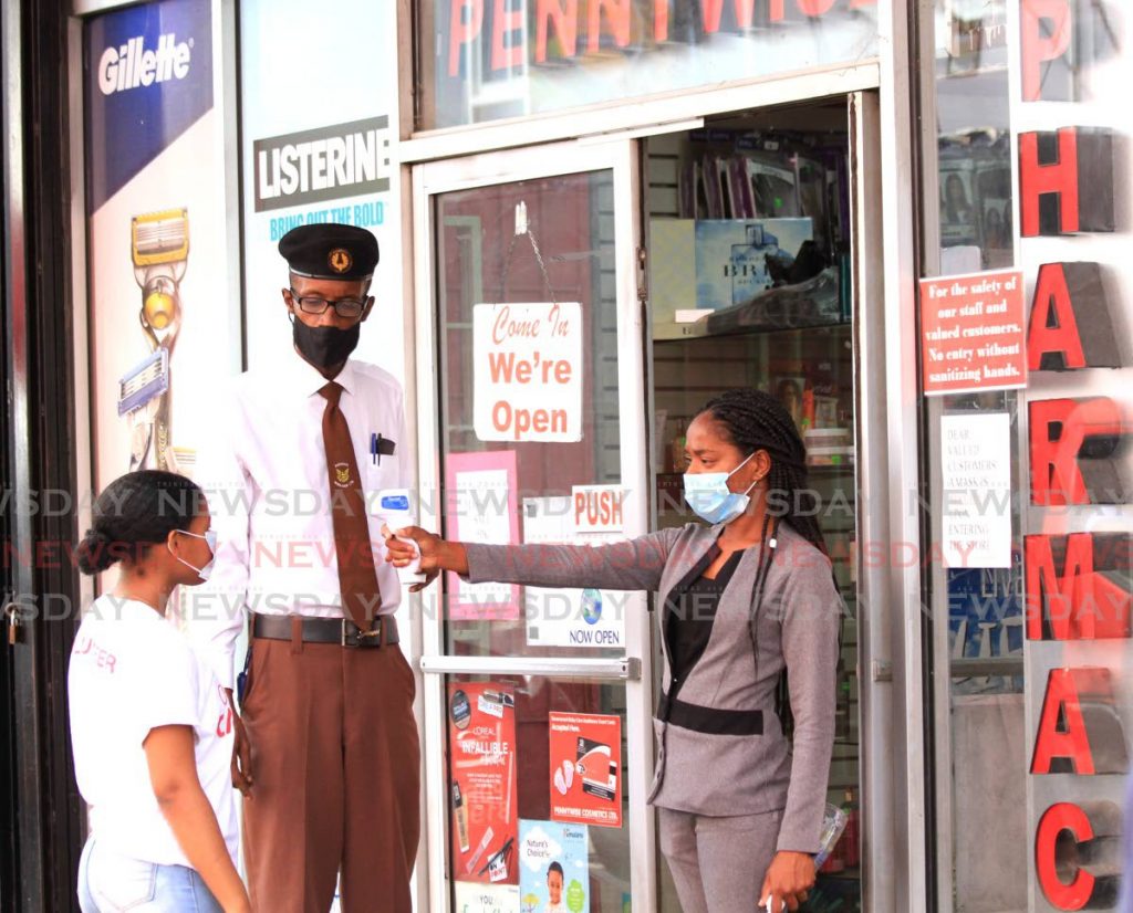 HEAT CHECK: A Pennywise Cosmetics worker, right, checks the temperature of a customer on Thursday at the entrance to the Charlotte Street, Port of Spain branch of the store.  - Ayanna Kinsale