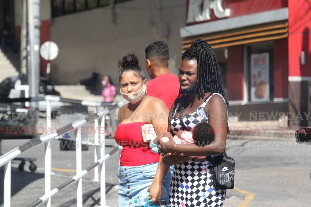 A woman carries a baby without wearing a mask, while another wears one beneath her nose, as they walk on High Street, San Fernando on Saturday. PHOTO BY LINCOLN HOLDER - 