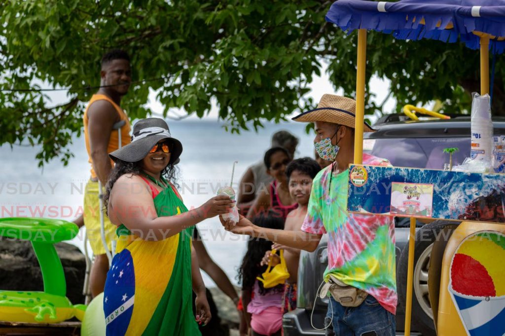 Snow cone vendor Anthony Hildinger, right, sells the sweet treat to a customer at Pigeon Point Beach, Tobago on August 16, one day before the closure of beaches and rivers as part of new government restrictions to curb the covid19 spread. Movement between Tobago and Trinidad is now restricted to essential travel which Tobago hoteliers said has led to a shut down of domestic tourism. - DAVID REID 