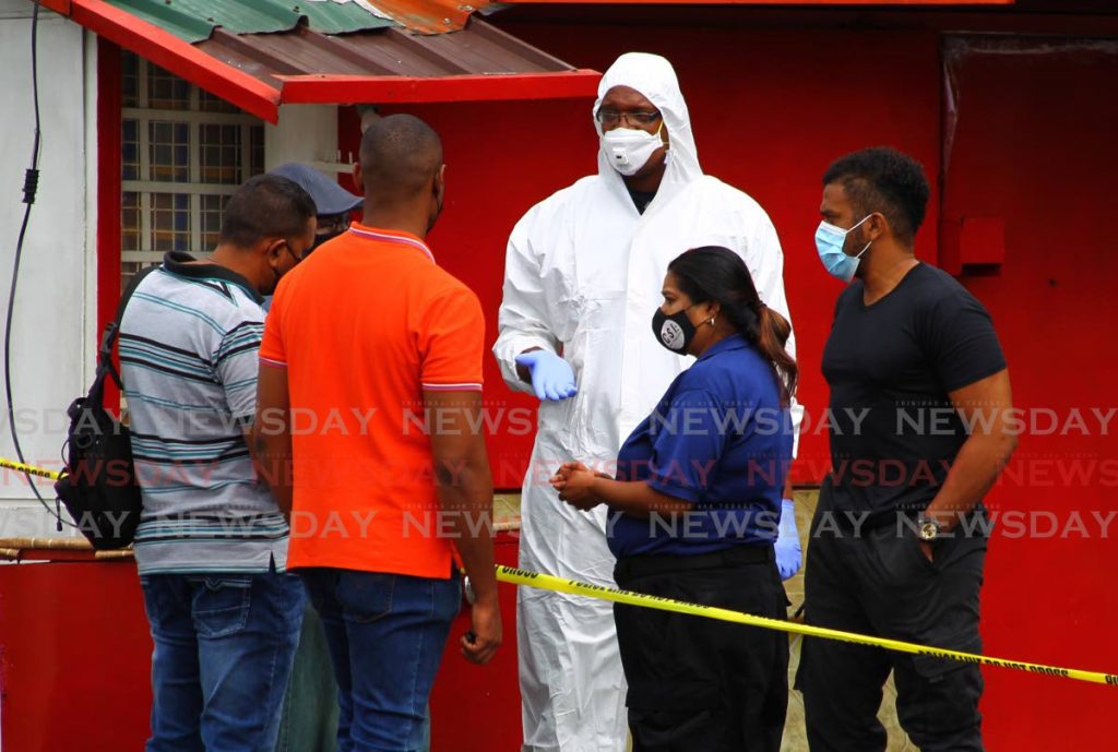 Crime scene investigators gather in discussion outside Happiness Supermarket at the corner of Eastern Main Road and Sixth Avenue, Barataria early Sunday morning. An Asian man was killed and six members of his family were wounded when they fought with eight bandits that tried to rob them at their home above the business place. - ROGER JACOB