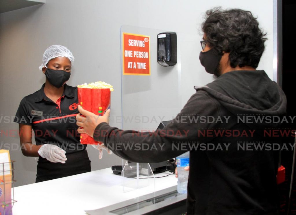 Customer Justin Baldeosingh receives his popcorn from CSR Melissa Garcia as Caribbean Cinemas 8 reopened for business  after the covid19 lockdown on June 25. Amcham applauds Government's management of the pandemic as it proposes ways for the country to go forward. - Ayanna Kinsale