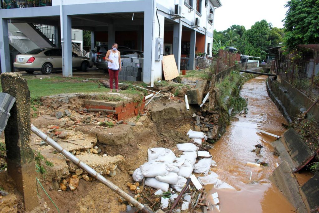 Arouca resident Hema Ganesh looks at where floodwater broke down her wall on the Eastern Main Road, Arouca, on Tuesday. - Angelo Marcelle