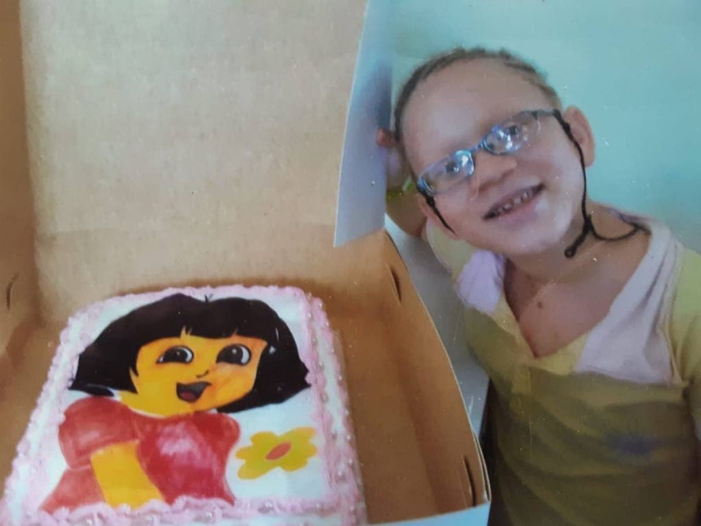 Shindlar Cuffy smiles while standing by the cake which was bought to celebrate her eighth birthday. - 