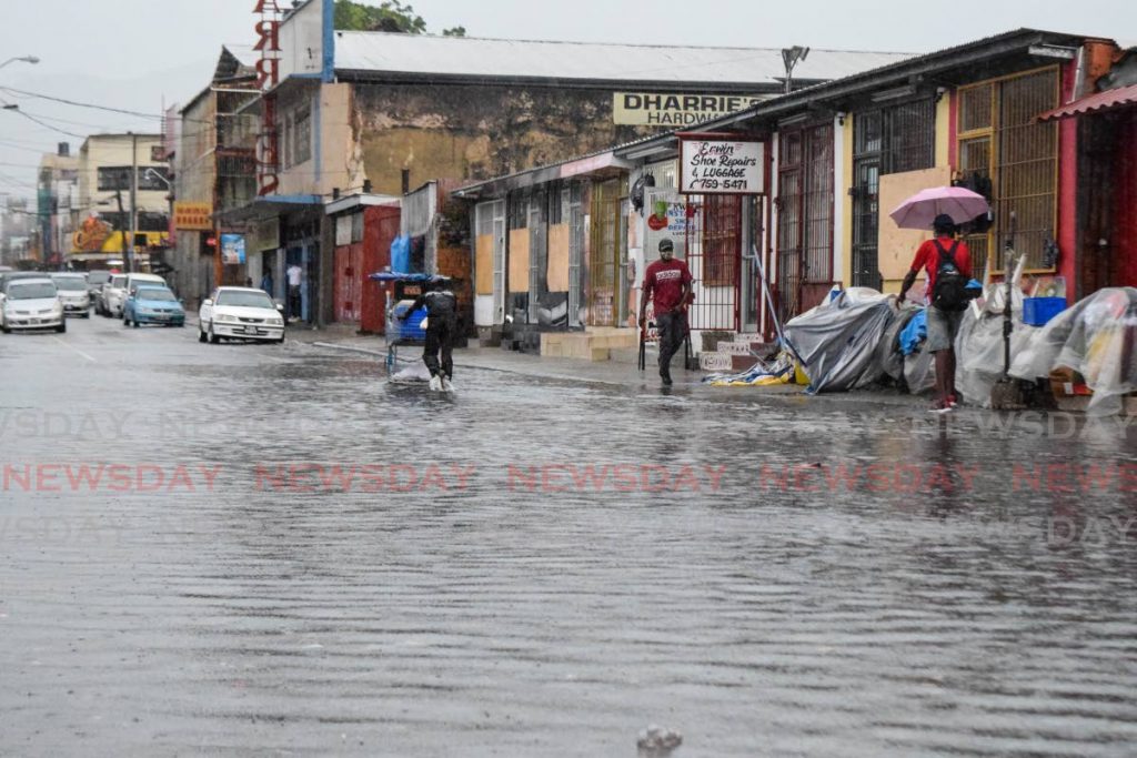 Pedestrians walk through floodwater on Henry Street, Port of Spain on Saturday morning. Torrential showers triggered flash flooding across Trinidad. - Vidya Thurab