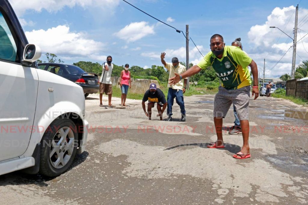 FED UP: Grants Road, Rousillac residents warn a driver about a pothole he was approaching as they protested the bad road condition on Thursday. - Marvin Hamilton