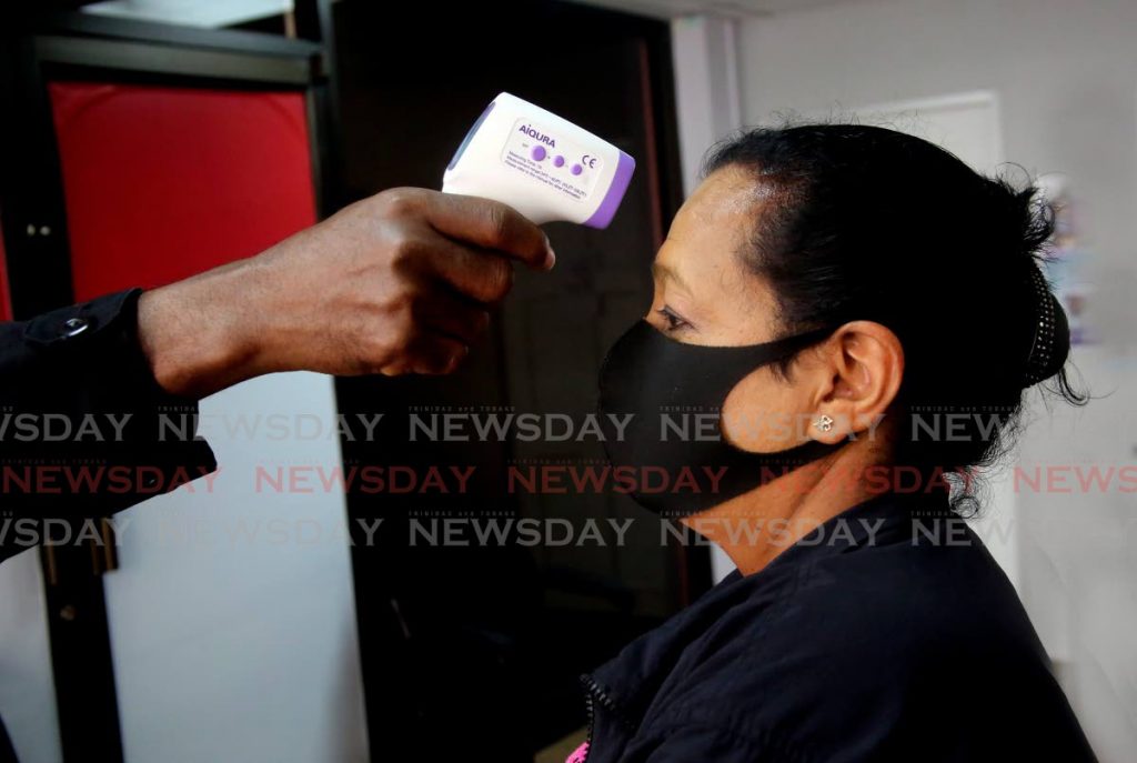 A woman's temperature is taken at an office in Port of Spain. Positive covid19 cases are declining public health officials said on Saturday. However deaths are up to 79. PHOTO BY SUREASH CHOLAI - 