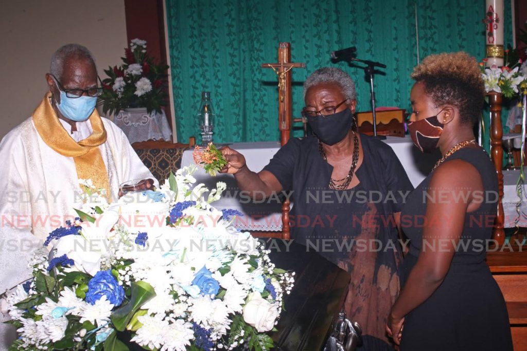 Julia Mc Milan-Jeffrey, centre, blesses the body of her husband Fitzgerald Jeffery, a former La Brea MP, alongside their daughter Tehilla Jeffery and Fr Wilfred John during his funeral at St Joseph RC Church, Vance River on Saturday morning. PHOTO BY CHEQUANA WHEELER 