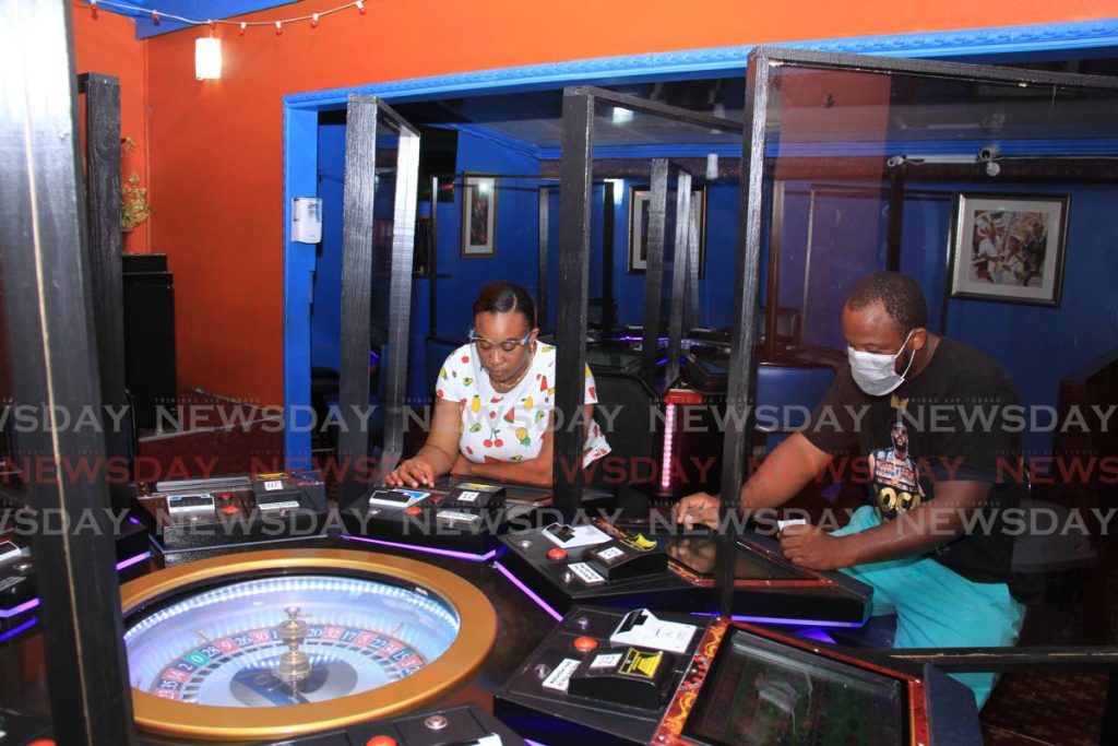 Jade Monkey Casino marketing manager Nickesha Nottingham, left, and machine technician Marlon Edwards at a roulette machine on Wednesday at the Crown Point establishment. Customers are now separated by Plexiglass to prevent the spread of covid19. PHOTO BY AYANNA KINSALE - 